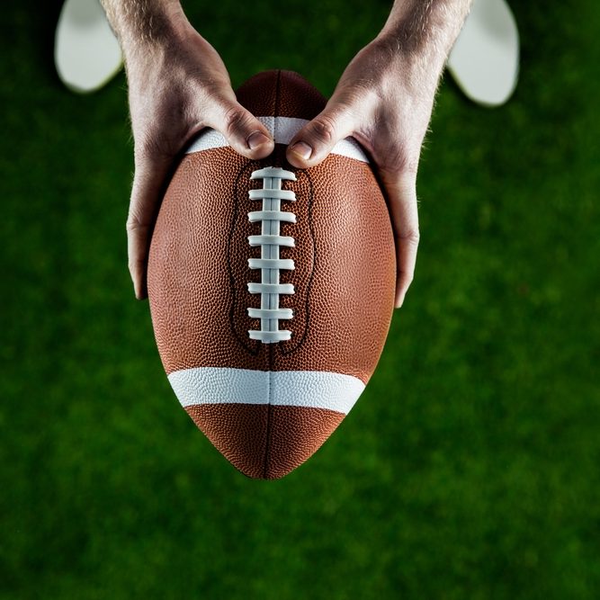 American football player holding up football on american football field